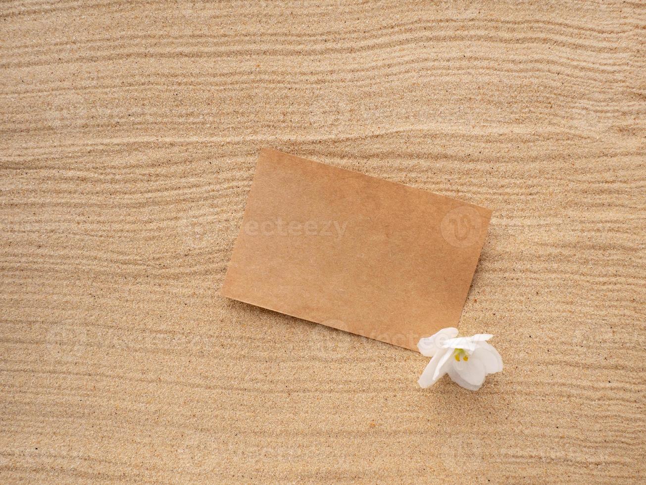 brief in de zand. ambacht papier met een wit Purper bloem Aan de structuur van zee zand. concept van een strand vakantie foto