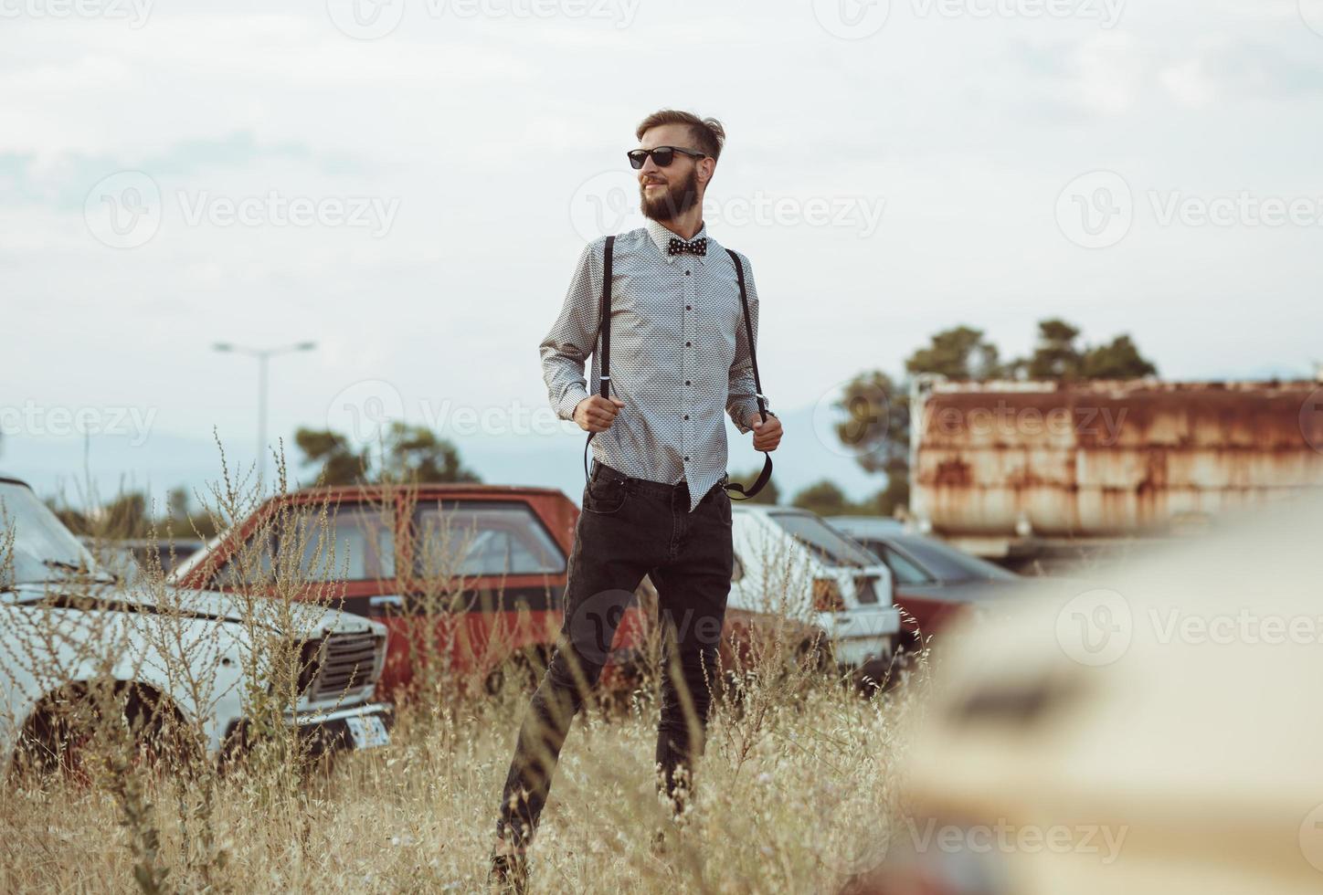 jong knap elegant Mens, vervelend overhemd en vlinderdas Aan de veld- van oud auto's foto