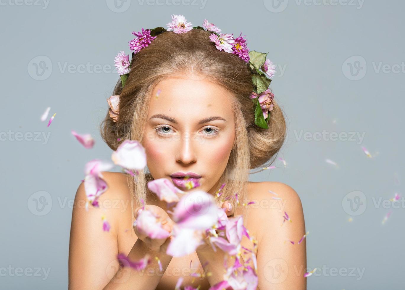 lief model- met glimmend volume gekruld haar- met bloemen, winter wit wimpers verzinnen, levendig lippen en roze wangen slagen bloemblaadjes met haar handen foto