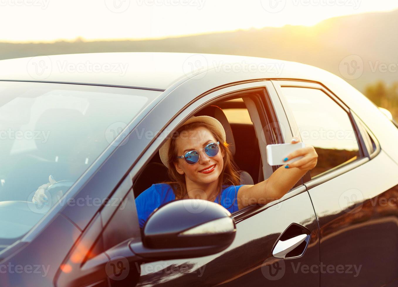 jong vrouw in hoed en zonnebril maken zelf portret zittend in de auto foto