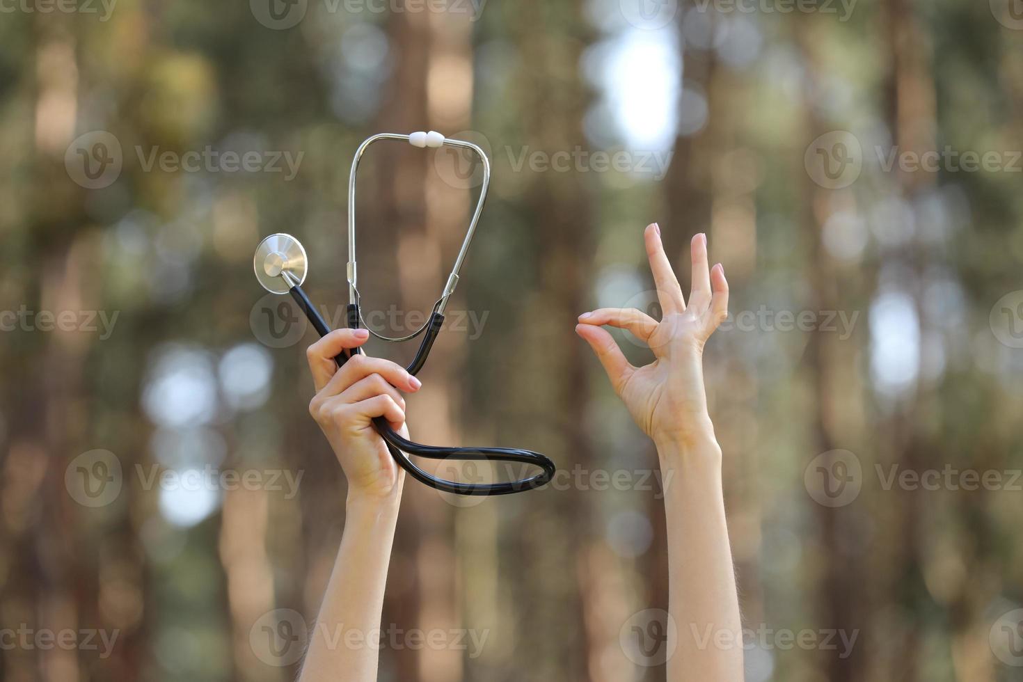 handen Holding een stethoscoop en tonen Oke teken Aan natuur Woud achtergrond foto