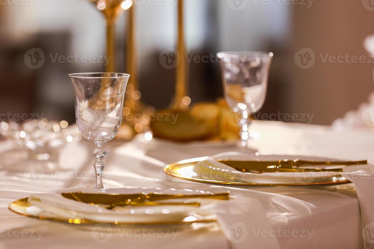 tafel decoratie met roze tafelkleed, kristal kandelaars met kaarsen en wit roze bloemen in restaurant . elegant bruiloft dag. instelling tafel met goud bord, vork en mes foto