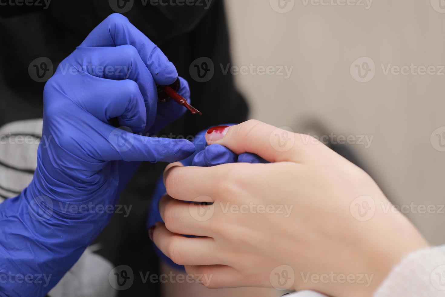 meester in beschermende handschoenen tijdens een manicure bij schoonheidssalon. meester-manicurist vernist de marsala-gel op de nagels van een vrouwelijke cliënt. het concept van schoonheid en gezondheid. foto