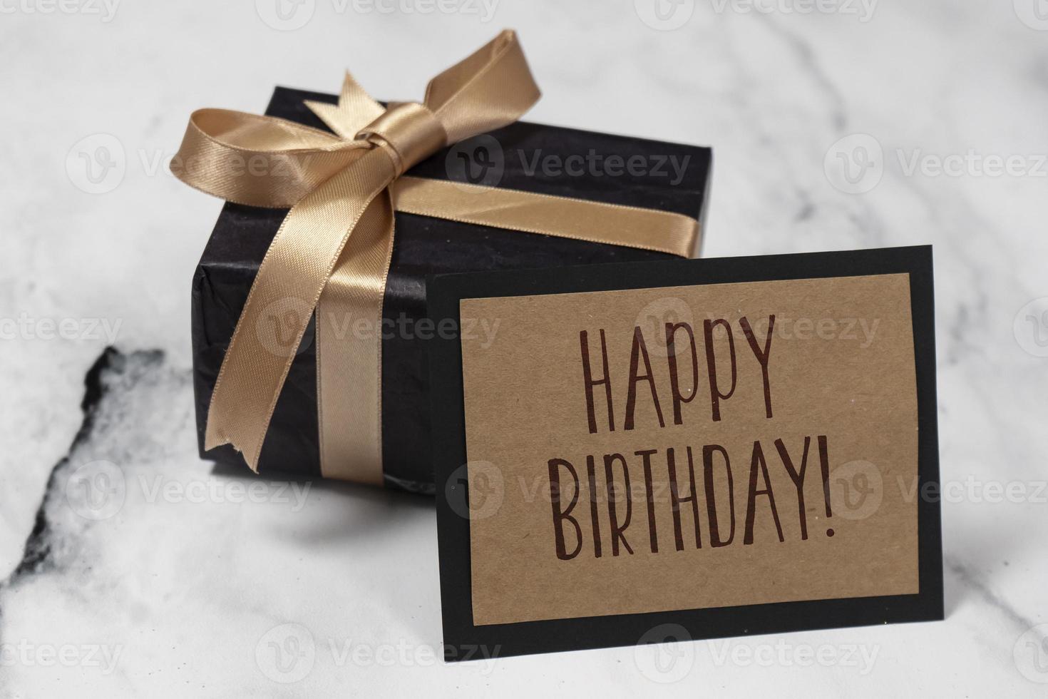 zwart geschenk doos met een gouden lint met een gelukkig verjaardag kaart Aan een wit en zwart marmeren tafel. foto