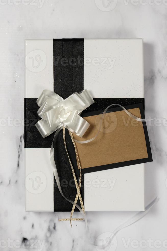 wit geschenk met zwart boog en leeg kaart Aan een wit en zwart marmeren tafel met een beetje van schitteren foto