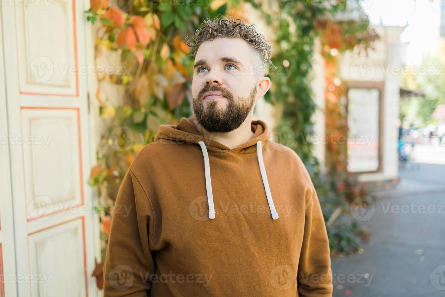 dichtbij omhoog schot van gekruld Europese mannetje met baard draagt wisselschot buitenshuis. knap Mens met knapperig licht haar. foto