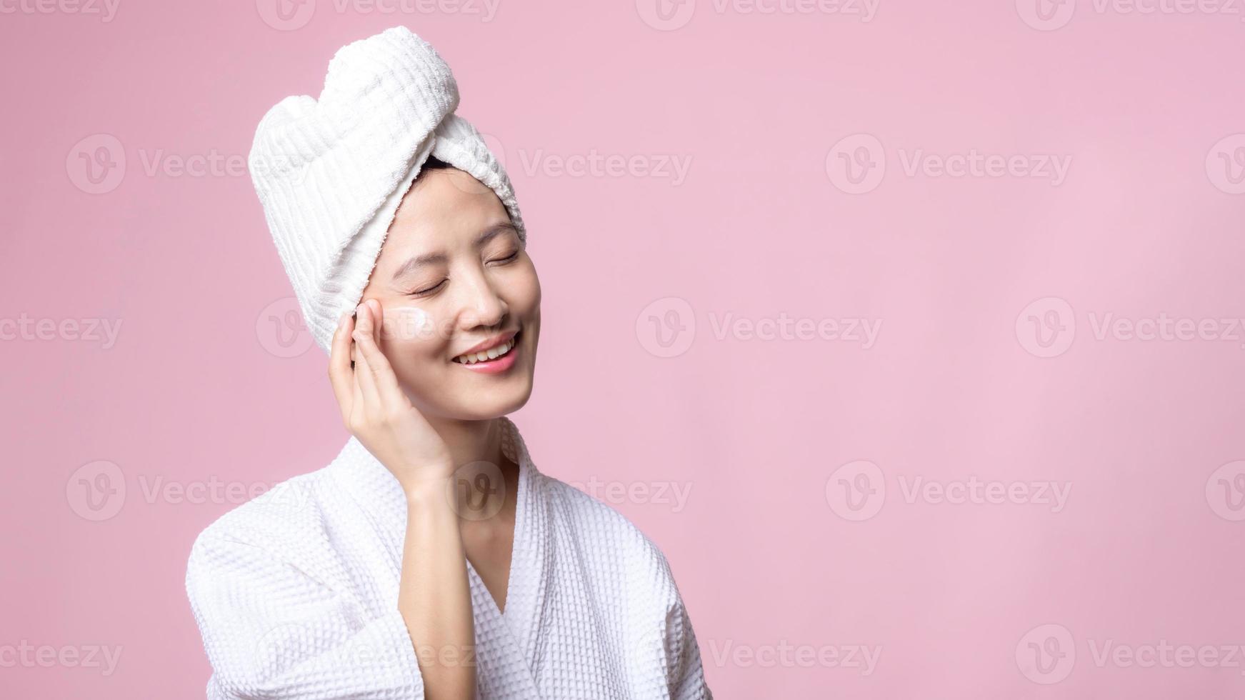 mooi jong Aziatisch vrouw gelukkig met schoon gezicht huid in handdoek en badjas, spa pak Aan roze achtergrond. huidverzorging, behandeling, welzijn therapie, gelaats zorg, schoonheid vrouw Gezondheid, schoonheidsspecialiste concept foto