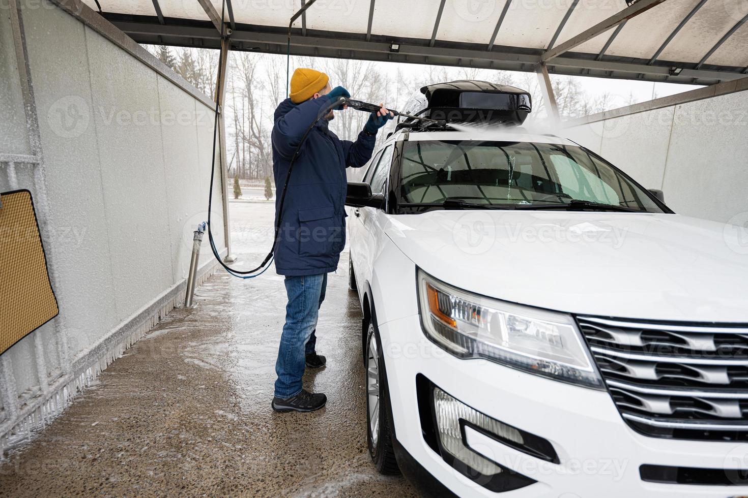 Mens het wassen hoog druk water Amerikaans suv auto met dak rek Bij zelf onderhoud wassen in verkoudheid het weer. foto