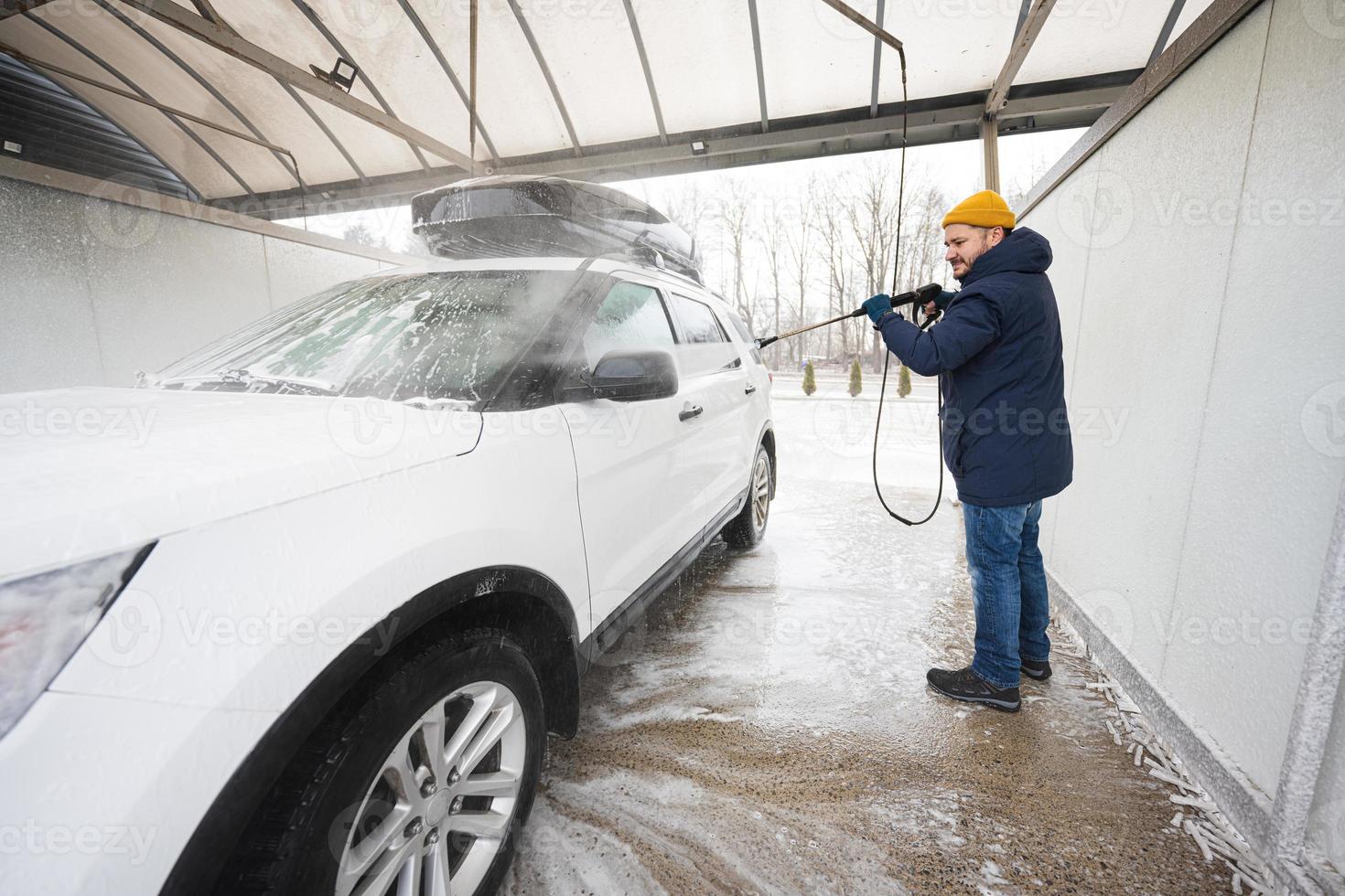 Mens het wassen hoog druk water Amerikaans suv auto met dak rek Bij zelf onderhoud wassen in verkoudheid het weer. foto