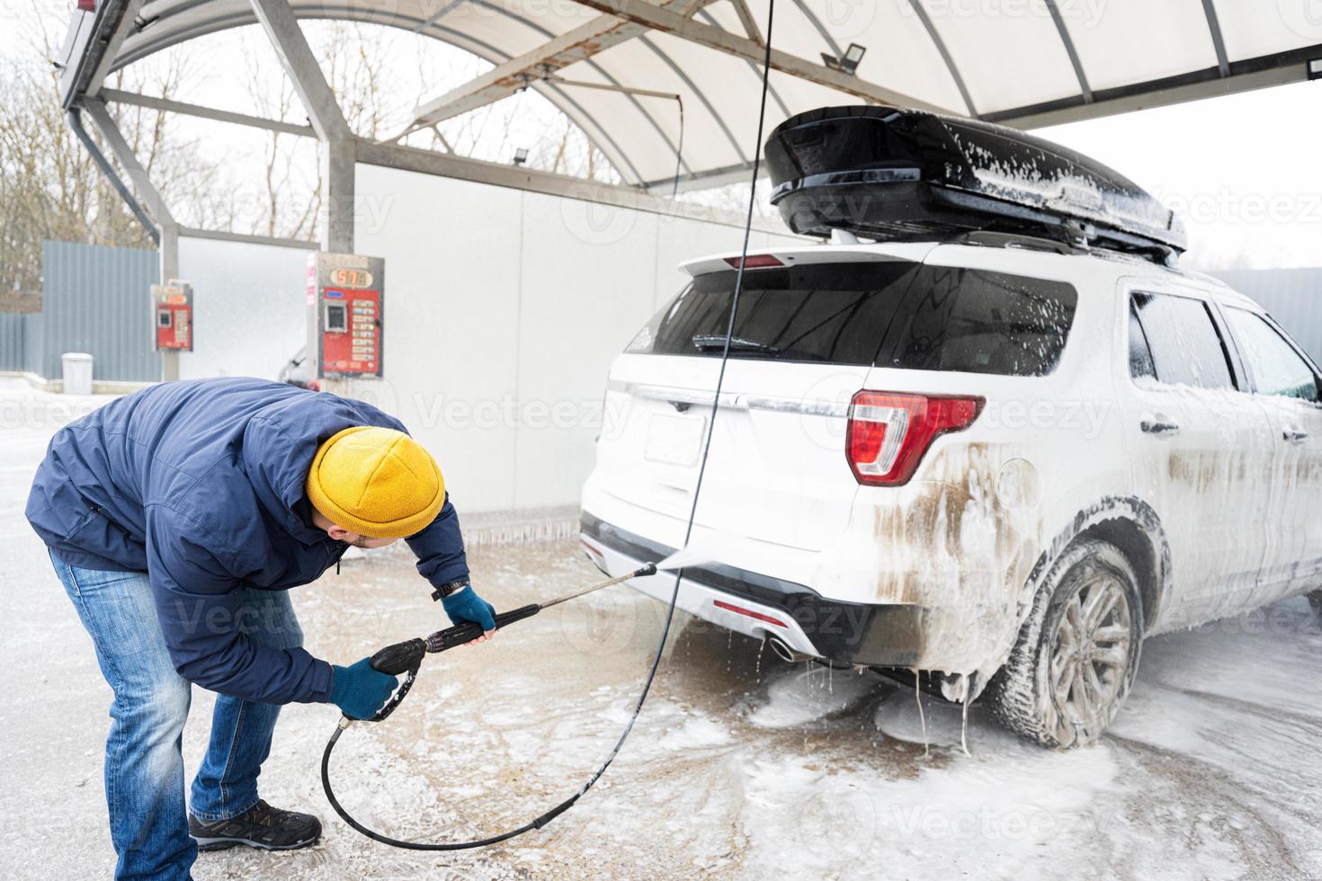 Mens het wassen hoog druk water Amerikaans suv auto met dak rek Bij zelf onderhoud wassen in verkoudheid het weer. foto