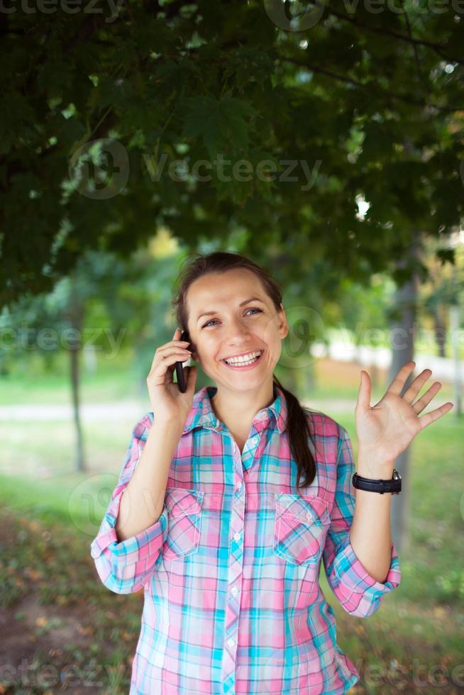 portret van een glimlachen vrouw in een park pratend Aan de telefoon foto