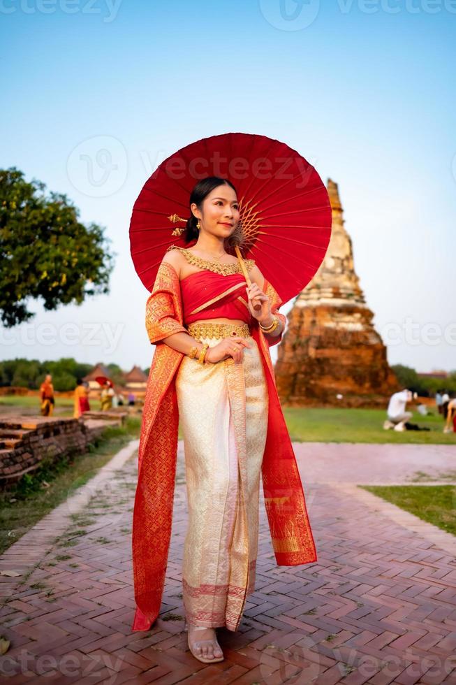 mooi Thais meisje in traditioneel jurk kostuum rood paraplu net zo Thais tempel waar is de openbaar plaats, Thais vrouw in traditioneel kostuum van Thailand. foto