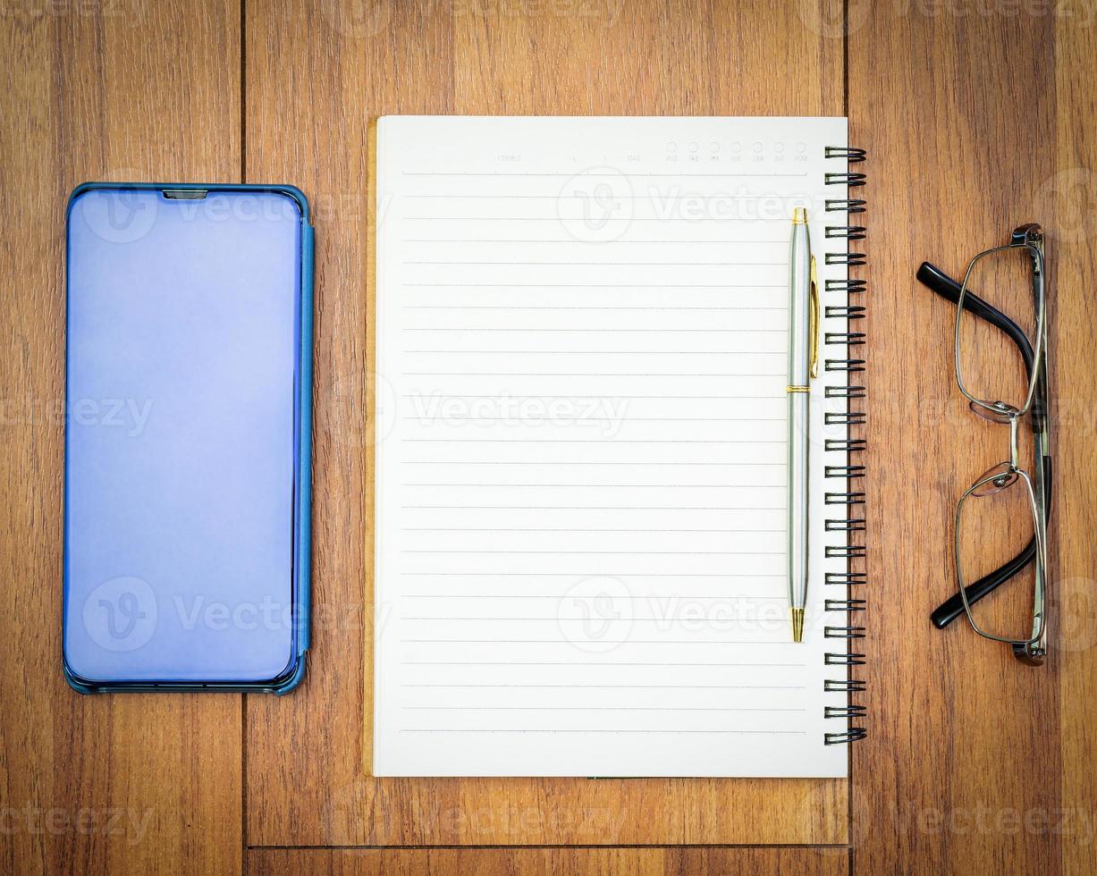bovenaanzicht afbeelding van open notebook met blanco pagina en mobiele telefoon op houten tafel foto