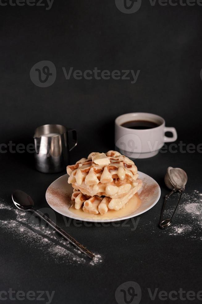 eigengemaakt van smakelijk belgisch wafels bord, karamel saus, koffie beker, melk Aan een zwart beton achtergrond foto