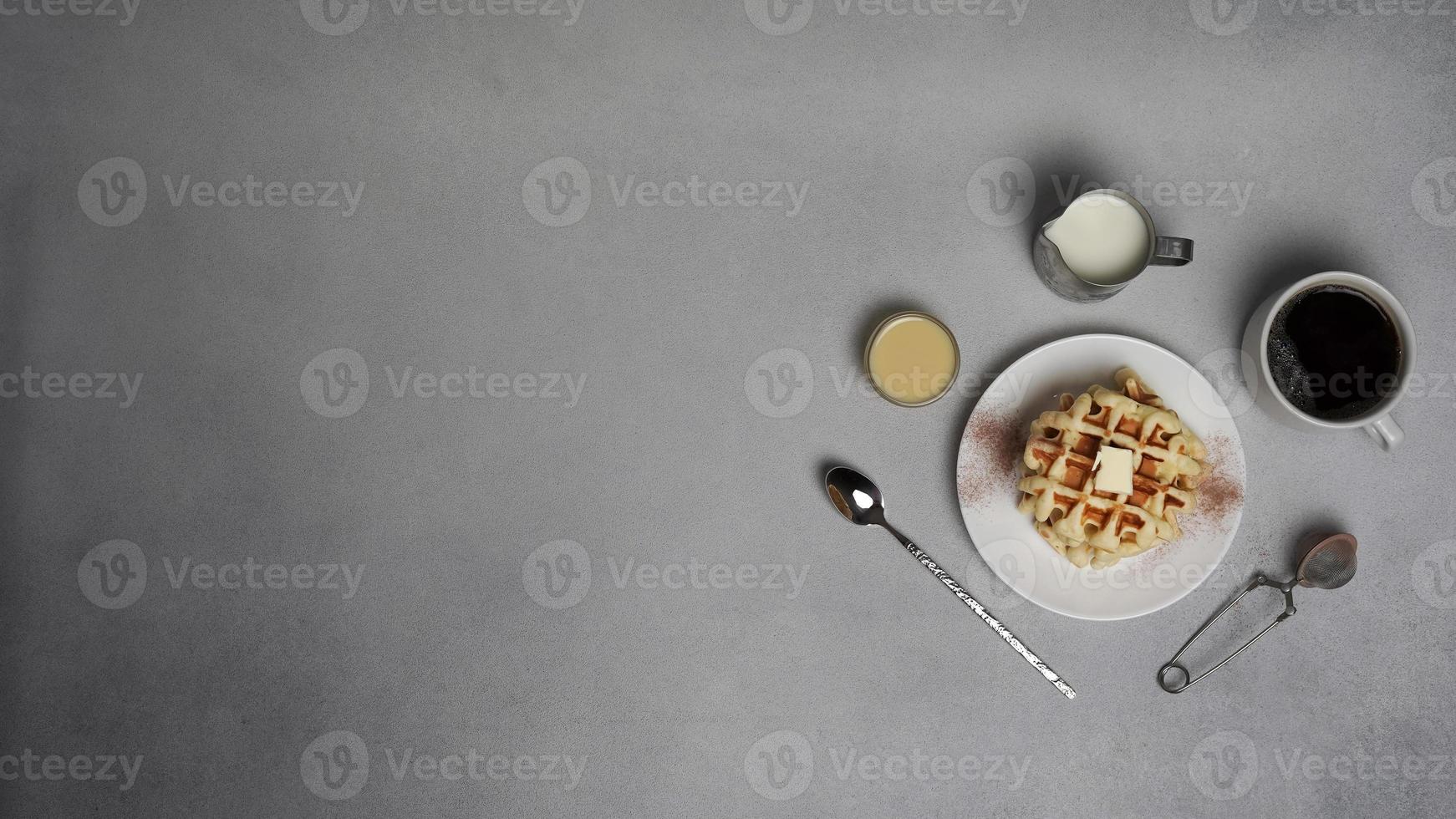 top visie van smakelijk wafels bord, karamel saus, koffie beker, melk, dessert lepel, zeef Aan een grijs beton achtergrond foto