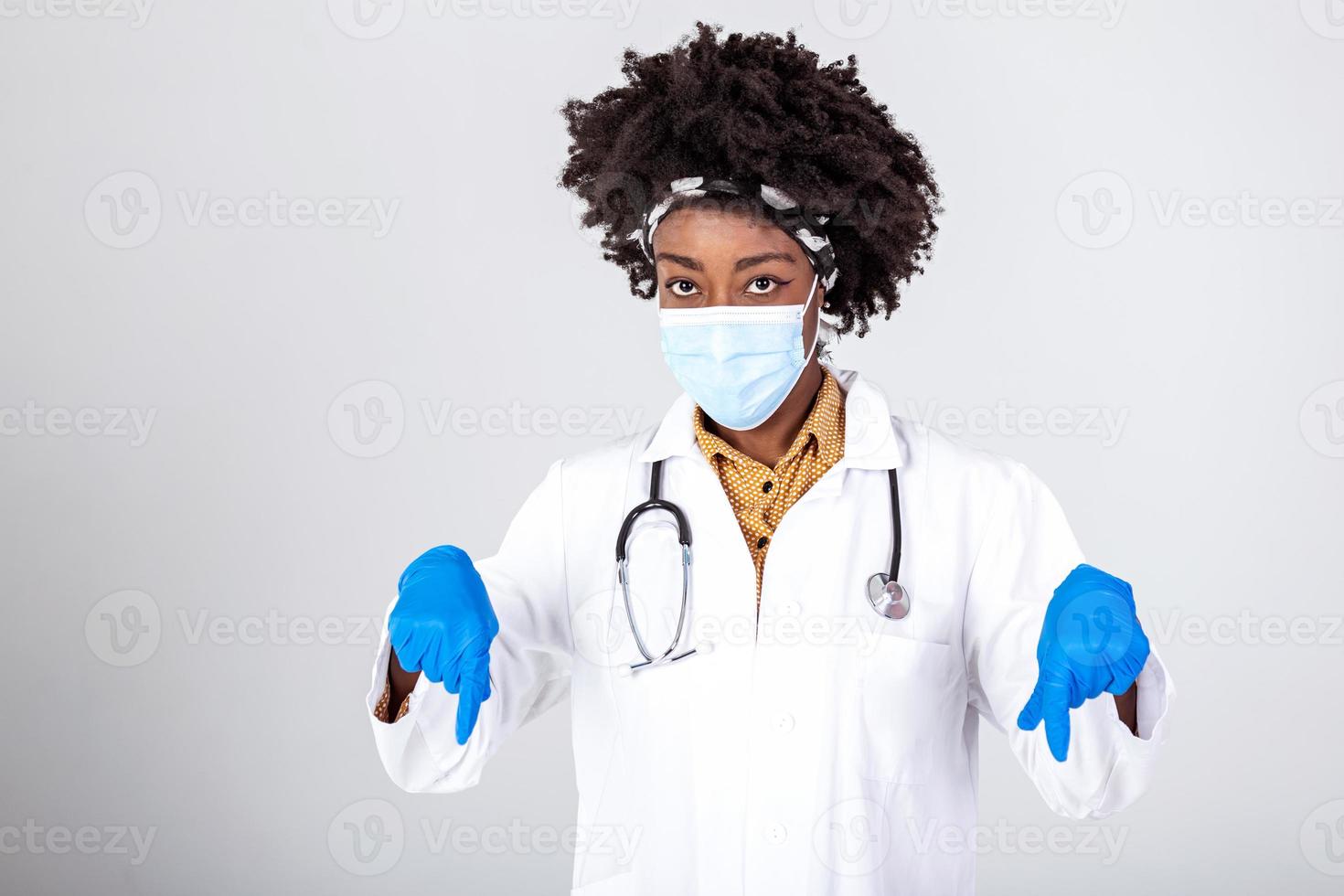 Afrikaanse Amerikaans dokter vrouw vervelend medisch masker en uniform richten vingers omlaag. geïsoleerd vrouw portret. foto