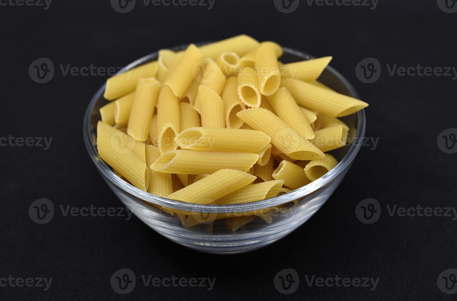 tarwe pasta in een glas kom Aan een zwart achtergrond. droog pasta in een transparant container. foto