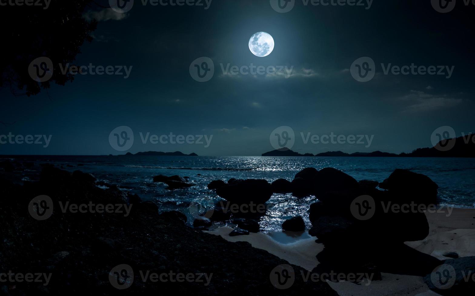 nacht Bij mooi strand met rotsen. rustig avond over- oceaan met vol maan foto