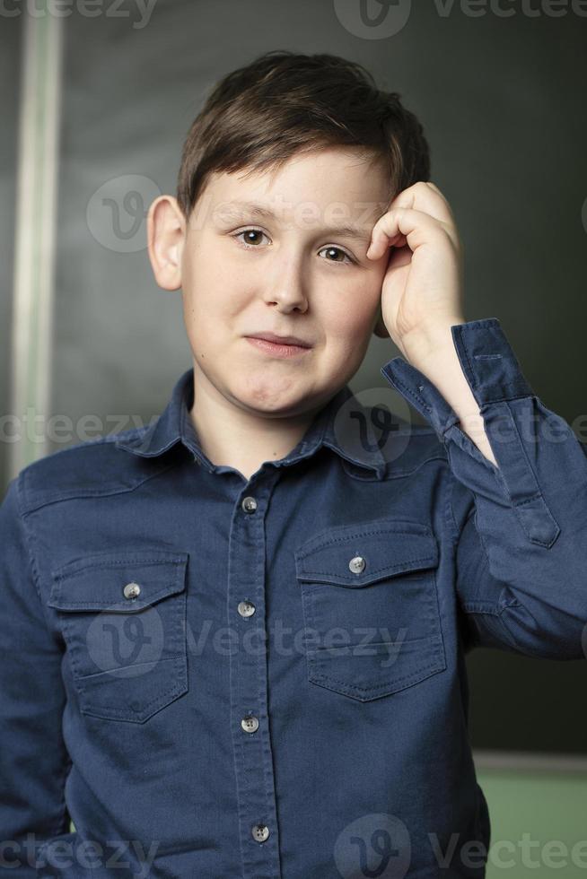 portret van een grappig schooljongen Bij de schoolbord. hij krassen zijn hoofd en niet weten de antwoord naar de vraag. foto