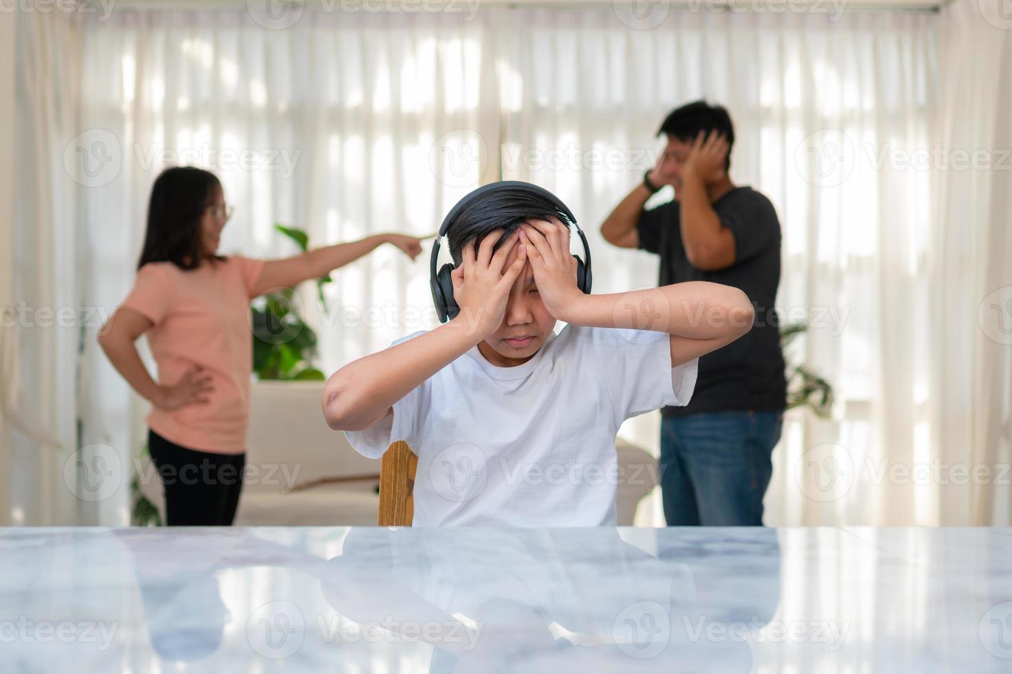 aziatische jongen die een koptelefoon draagt en luide muziek speelt. om geen ruzie te horen terwijl ouders ruzie of ruzie thuis hebben. ongelukkig probleem in het gezin, huishoudelijke problemen in het gezin. foto