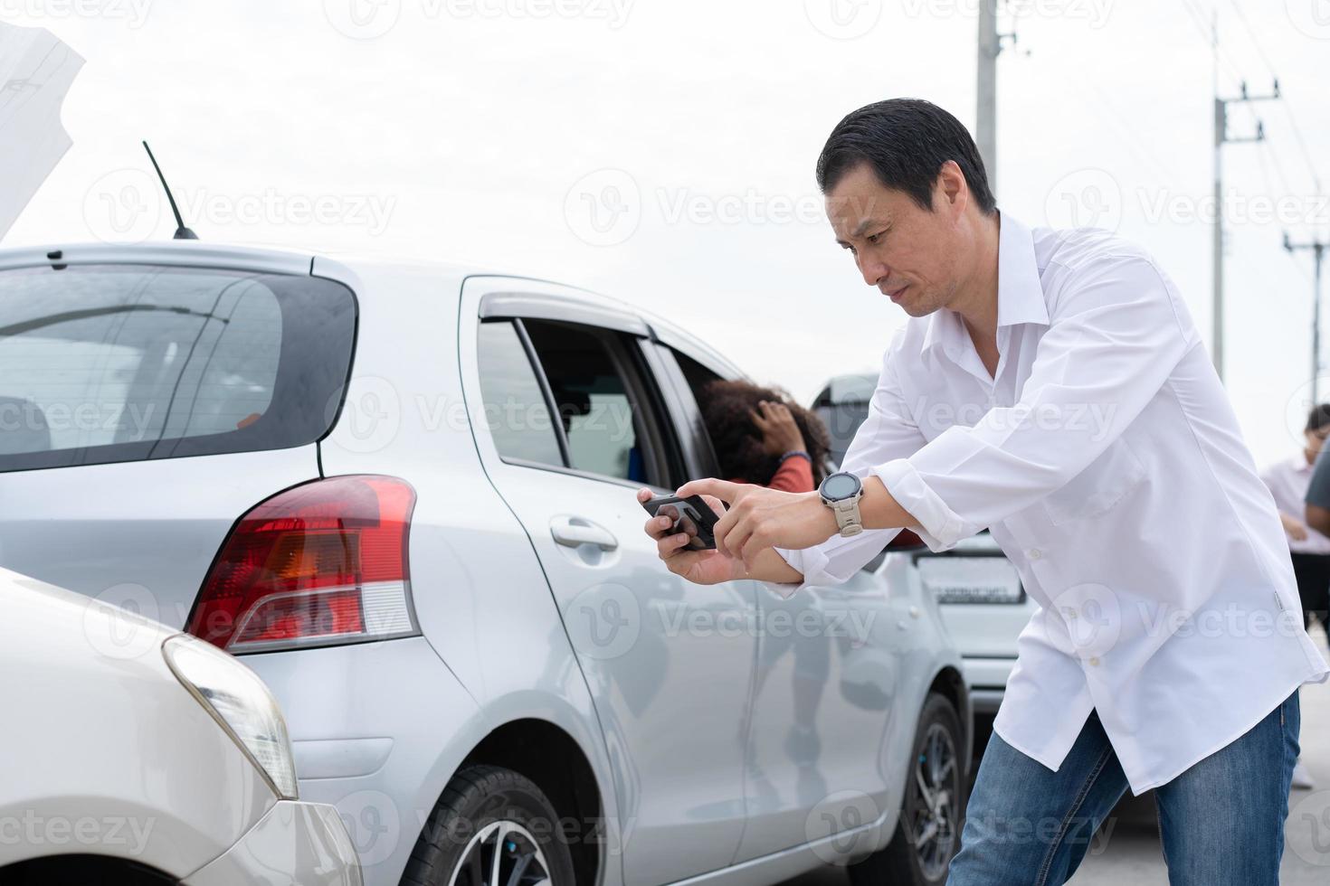 Aziatisch mannen bestuurder controleren voor schade na een auto ongeluk voordat nemen afbeeldingen en Bezig met verzenden verzekering. online auto ongeluk verzekering beweren na indienen foto's en bewijs naar een verzekering bedrijf. foto