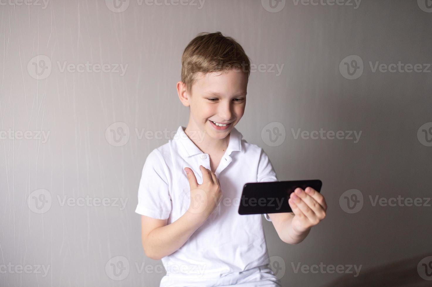 een jongen in een wit t-shirt met een zwart telefoon communiceert via video babbelen foto