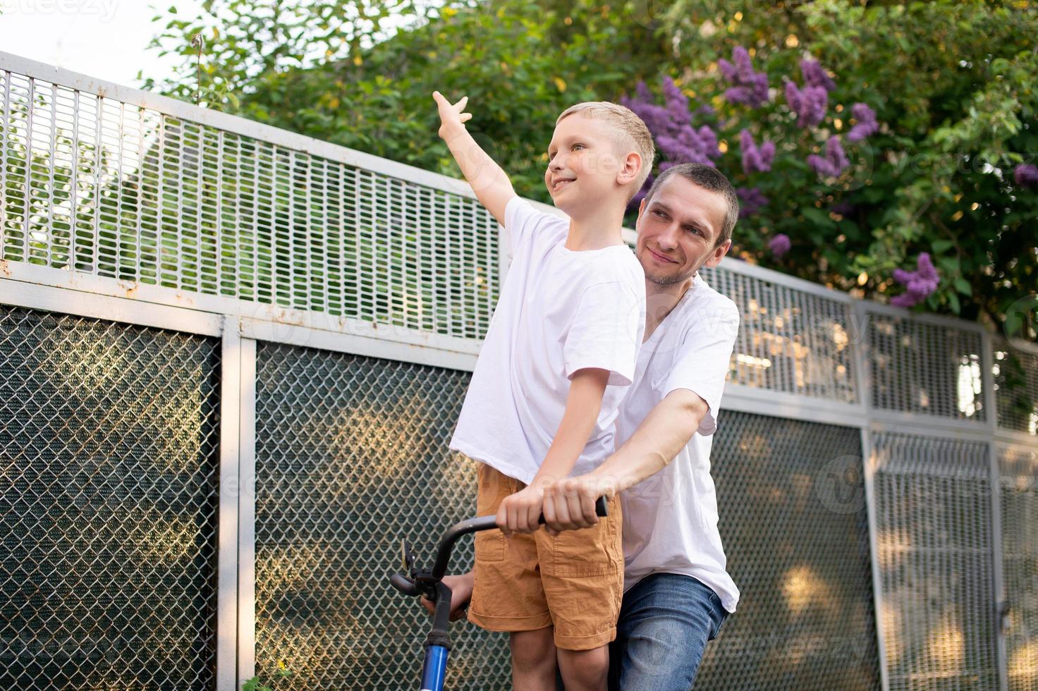 een schattig jongen in een wit t-shirt ritten een fiets met zijn vader en lacht. foto