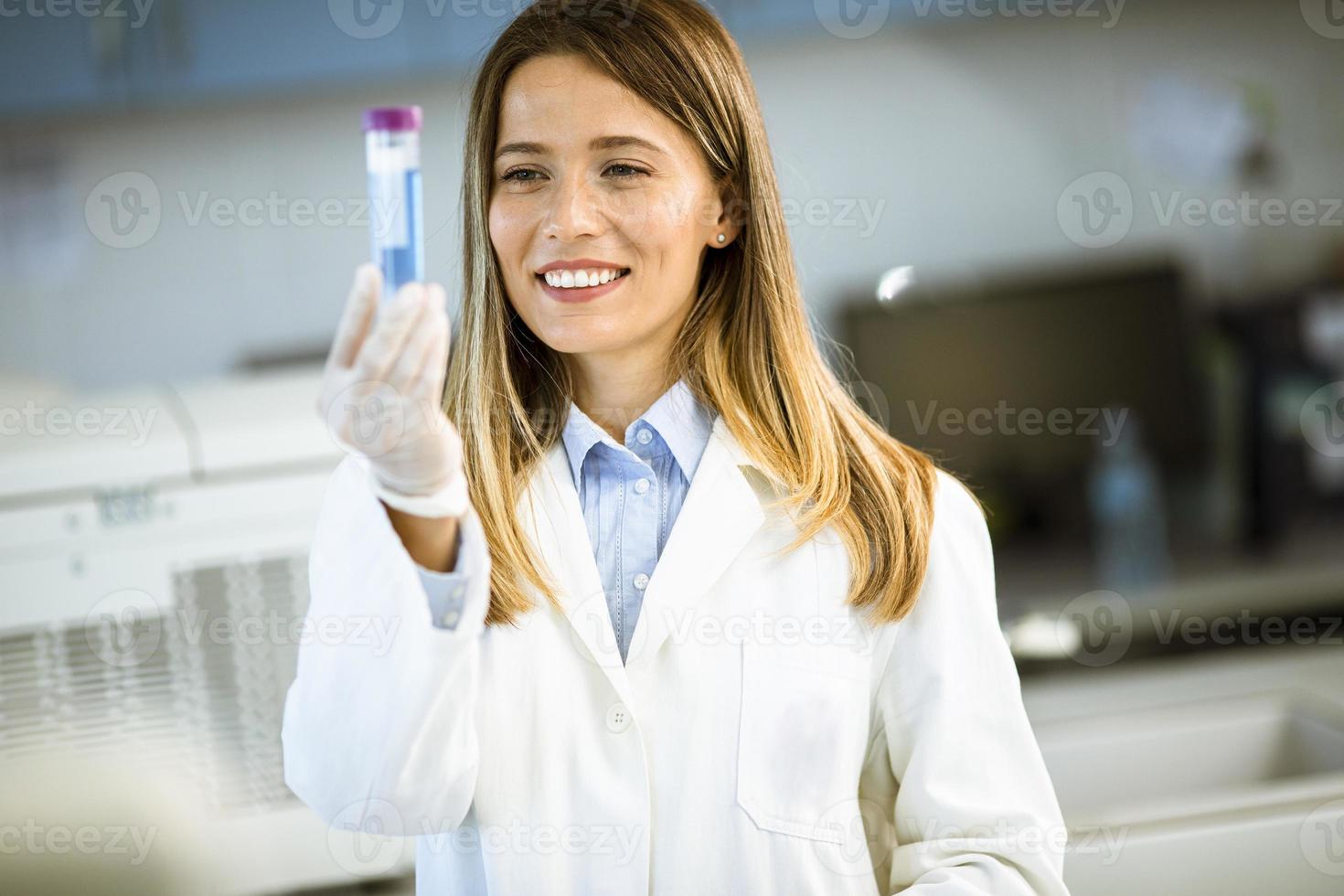 vrouwelijke arts die beschermend gezichtsmasker draagt in de kolf van de laboratoriumholding met vloeibaar monster foto