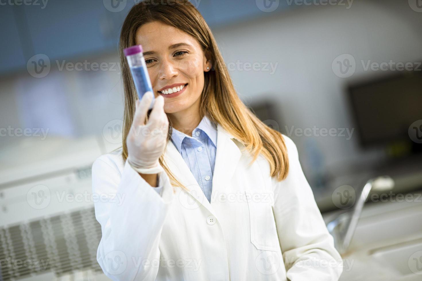 vrouwelijke arts die beschermend gezichtsmasker draagt in de kolf van de laboratoriumholding met vloeibaar monster foto