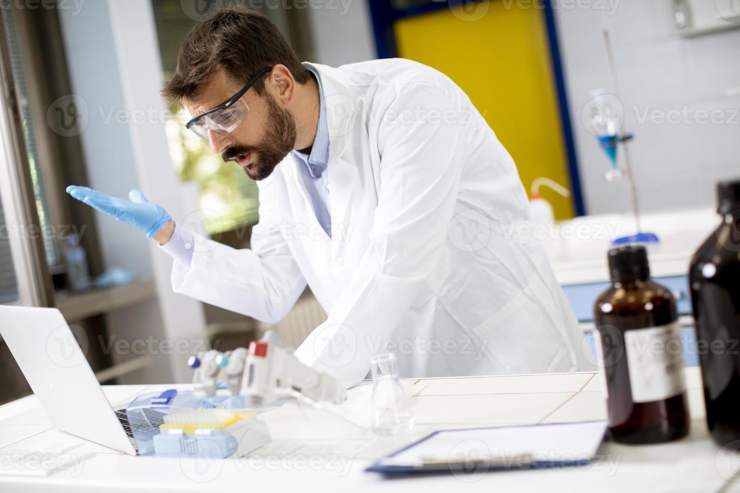 onderzoeker in witte laboratoriumjas werken met laptop zittend in het lab foto