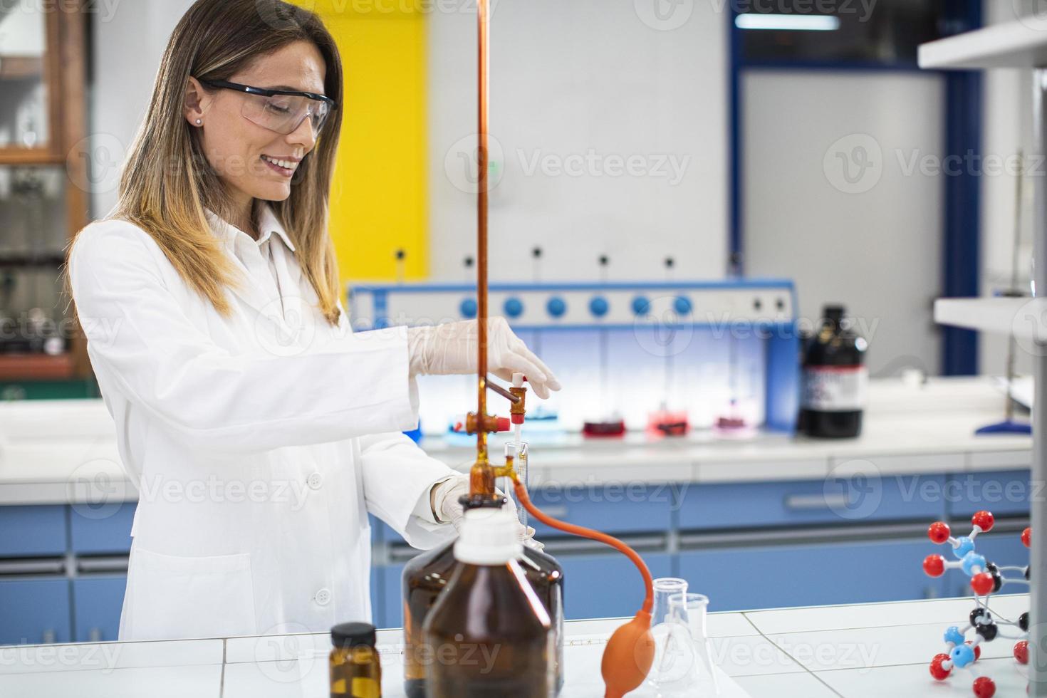 vrouwelijke onderzoeker in beschermende werkkleding permanent in het laboratorium en kolf met vloeibaar monster analyseren foto