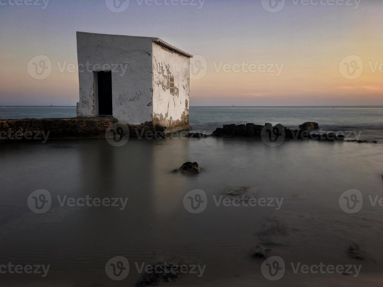 vissershut bij zonsondergang op enkele rotsen vlakbij het strand in calpe, alicante foto