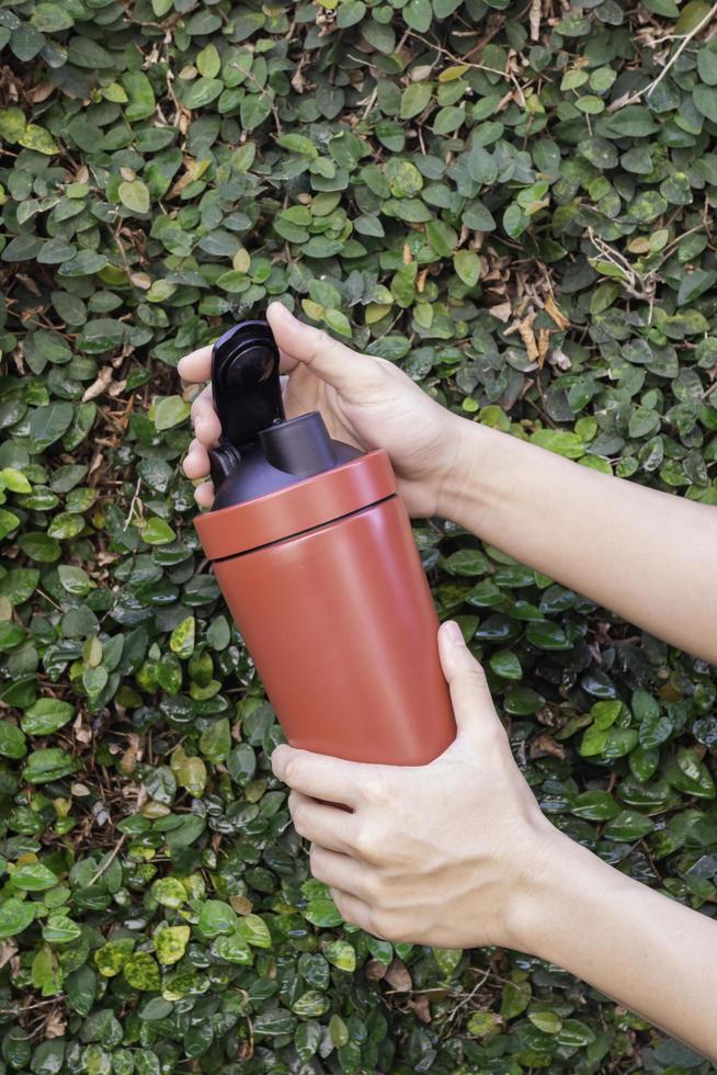 aluminium thermos mok in handen met groene bladeren muur achtergrond foto