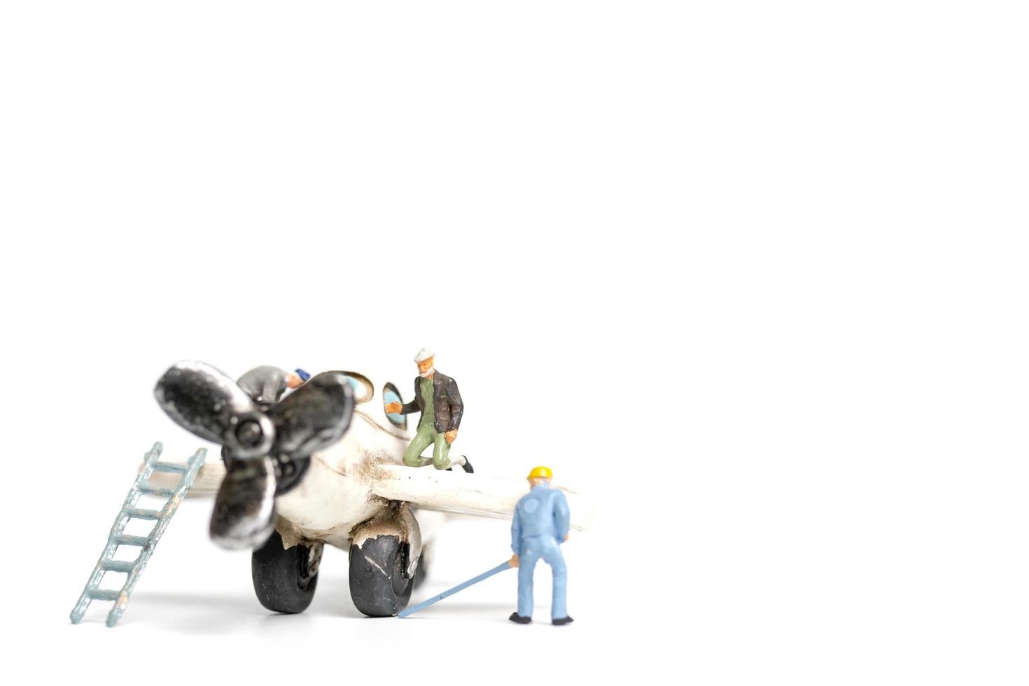 miniatuurarbeiders die een stuk speelgoed vliegtuig op een witte achtergrond herstellen foto