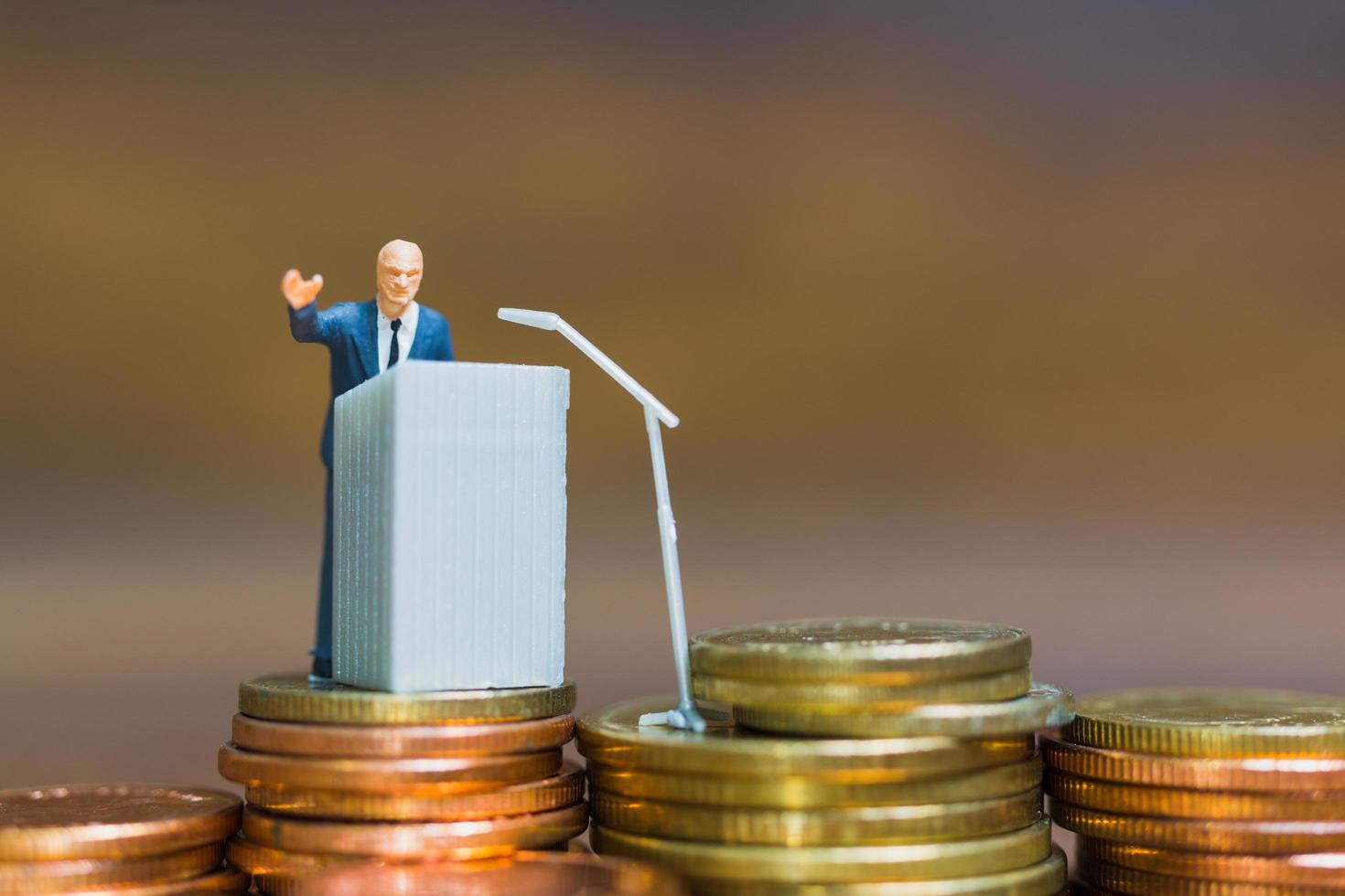 miniatuurzakenman die op een podium op een stapel muntstukken, bedrijfs en financieel investeringsconcept spreekt foto