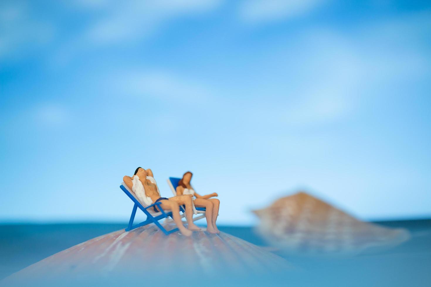 miniatuurmensen die op een zeeschelp met een blauwe hemelachtergrond zonnebaden, het concept van de zomervakantie foto
