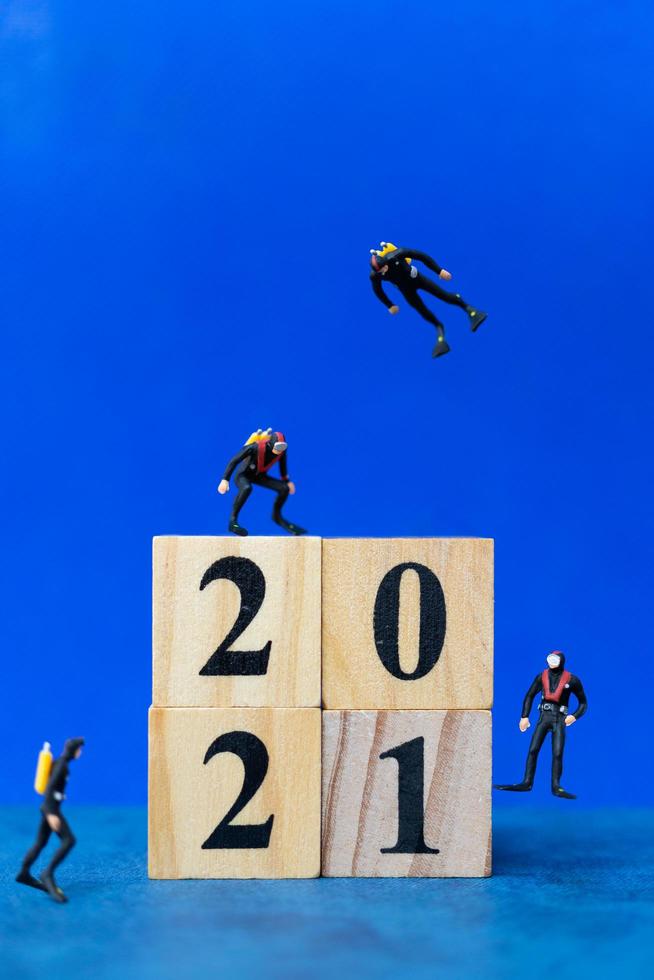 miniatuurduikers die rond houten blokken duiken met het nummer 2021, gelukkig nieuwjaarsconcept foto