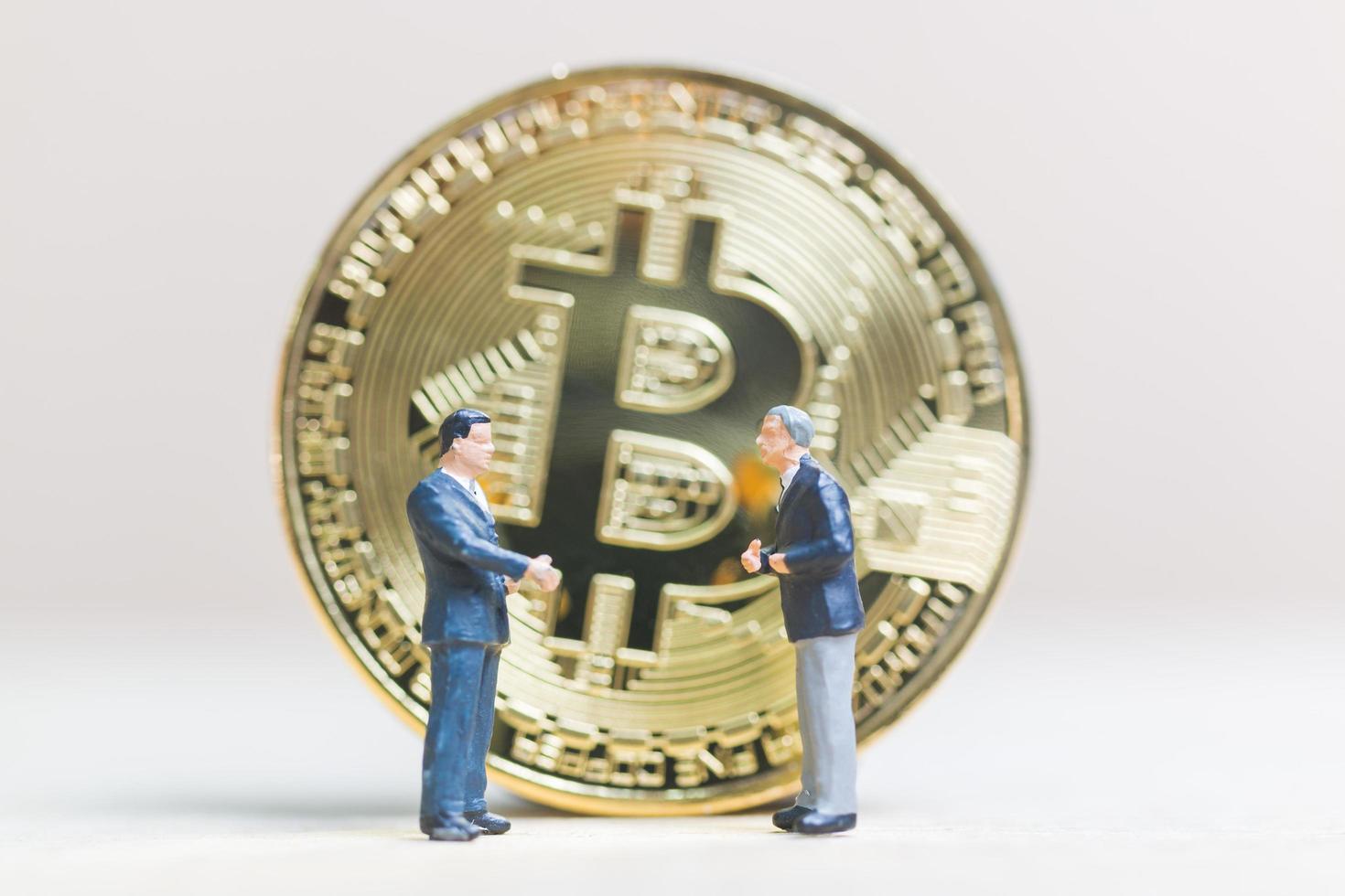 miniatuurzakenlieden die zich voor een bitcoin cryptocurrency-muntstuk bevinden, bedrijfsconcept foto