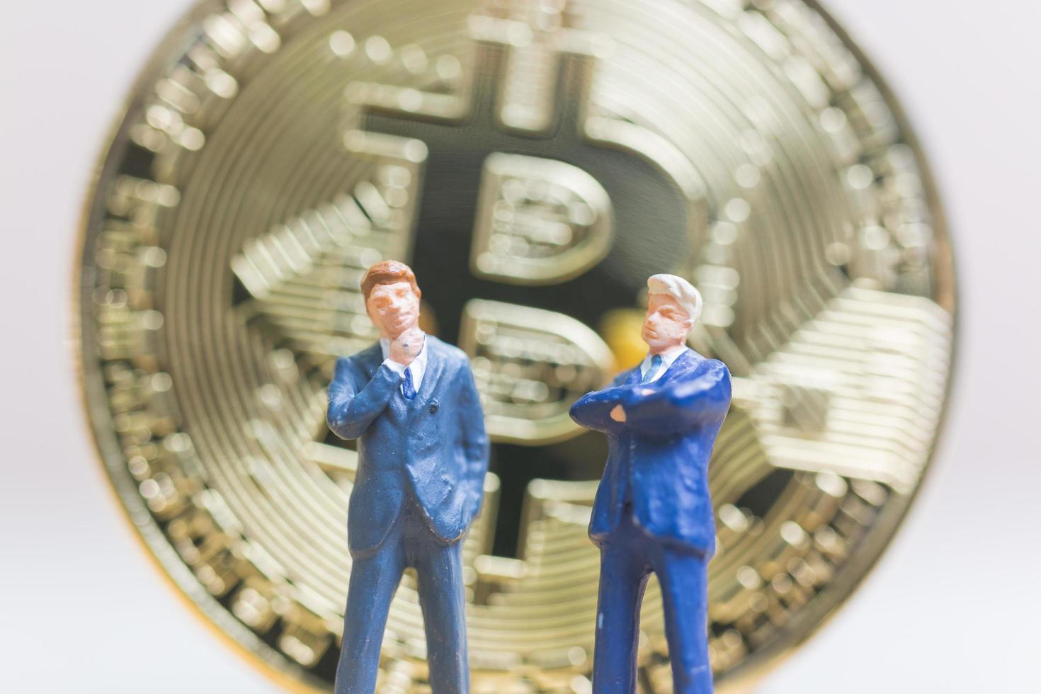 miniatuurzakenlieden die zich voor een bitcoin cryptocurrency-muntstuk bevinden, bedrijfsconcept foto
