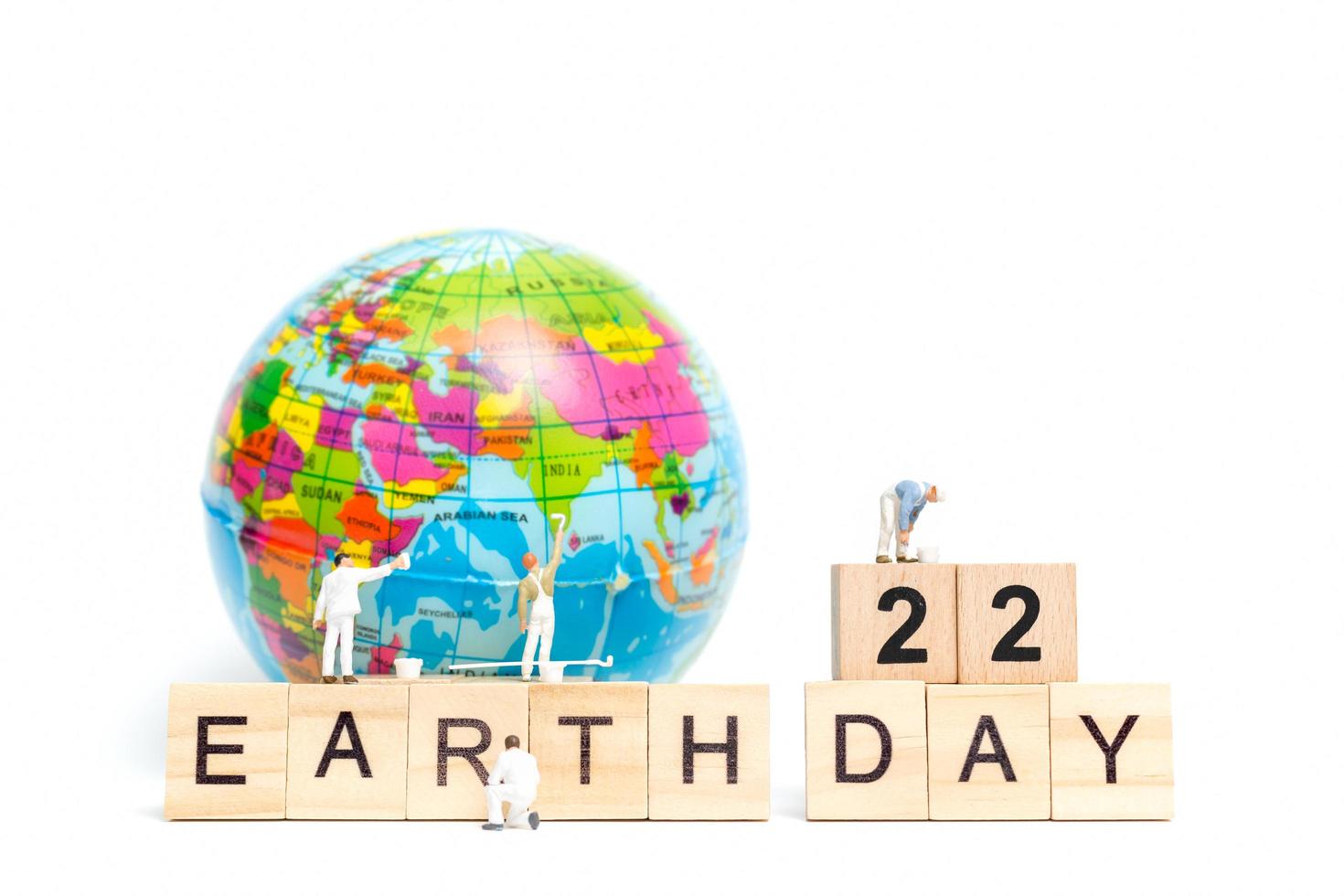 miniatuurschilders die op een wereldbol met houten blokken schilderen die dag 22 van de aarde op een witte achtergrond, het concept van de dag van de aarde tonen foto