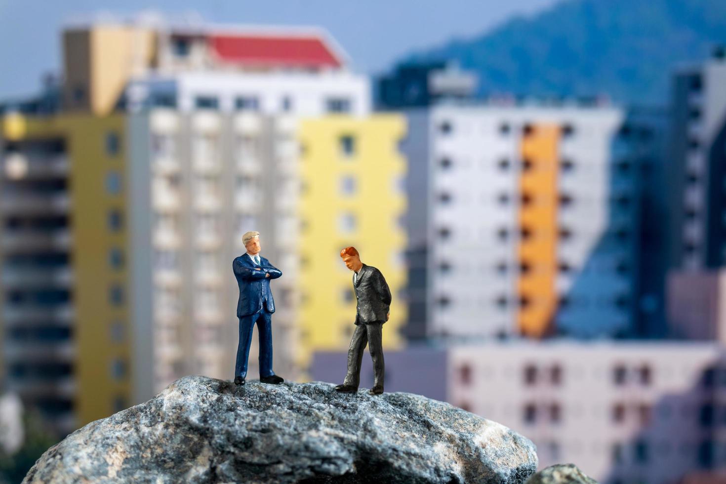miniatuurzakenlieden die zich op een rots met gebouwen op de achtergrond bevinden foto
