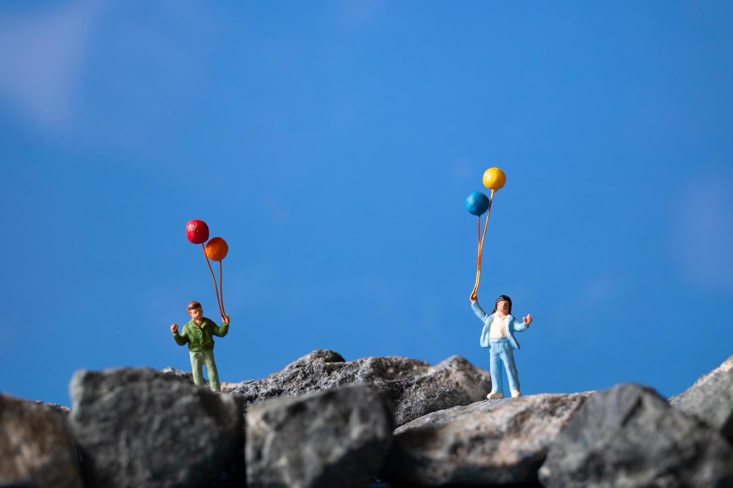 miniatuurfamilie met ballonnen op een rots met een blauwe hemelachtergrond foto