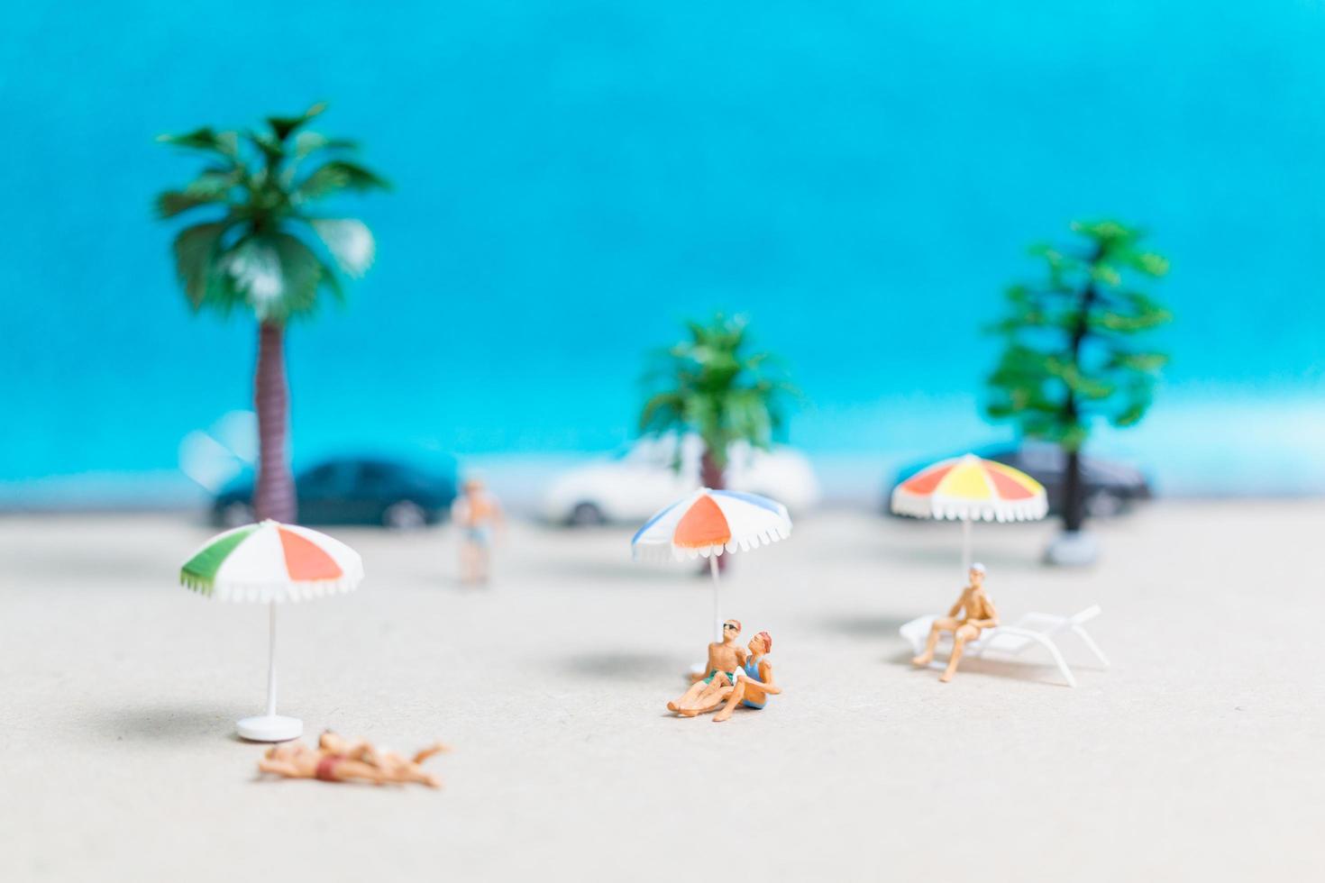 miniatuurmensen die zwemkleding dragen die op een strand met een blauwe achtergrond ontspannen foto