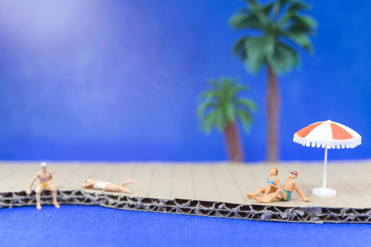 miniatuurmensen die zwemkleding dragen die op een strand met een blauwe achtergrond ontspannen foto