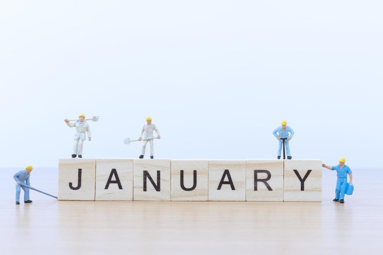 miniatuurmensen die aan houten blokken werken met het woord januari op een houten vloer foto