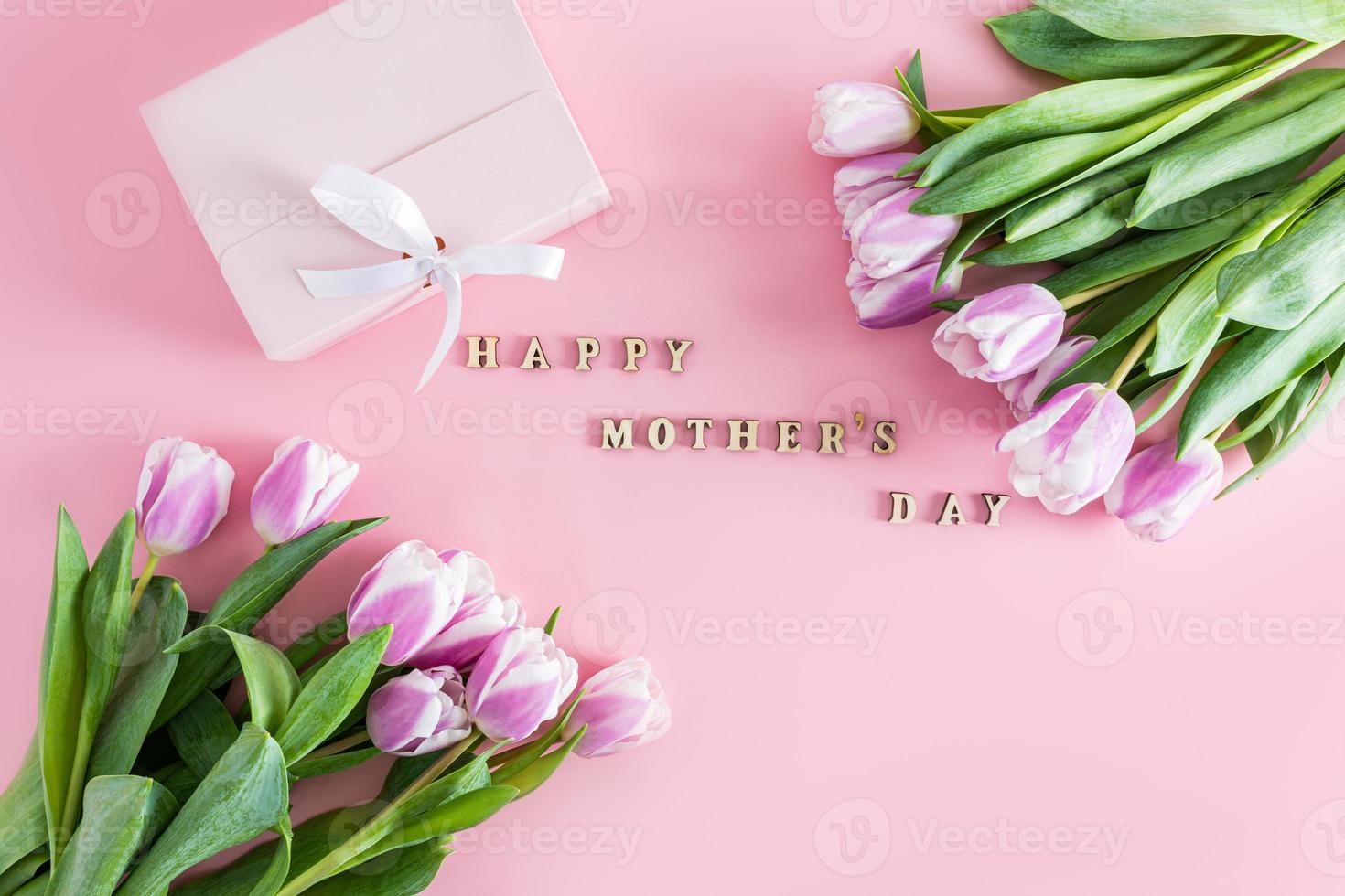 een feestelijk samenstelling met Purper tulpen en tekst in houten brieven van gelukkig moeder dag. top visie. vlak stileren. roze achtergrond. foto