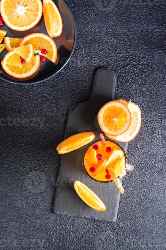 oranje veenbes koolzuurhoudend cocktail in een glas en fruit en bessen dichtbij Aan een leisteen Aan een donker achtergrond. eigengemaakt mocktail. top en verticaal visie foto