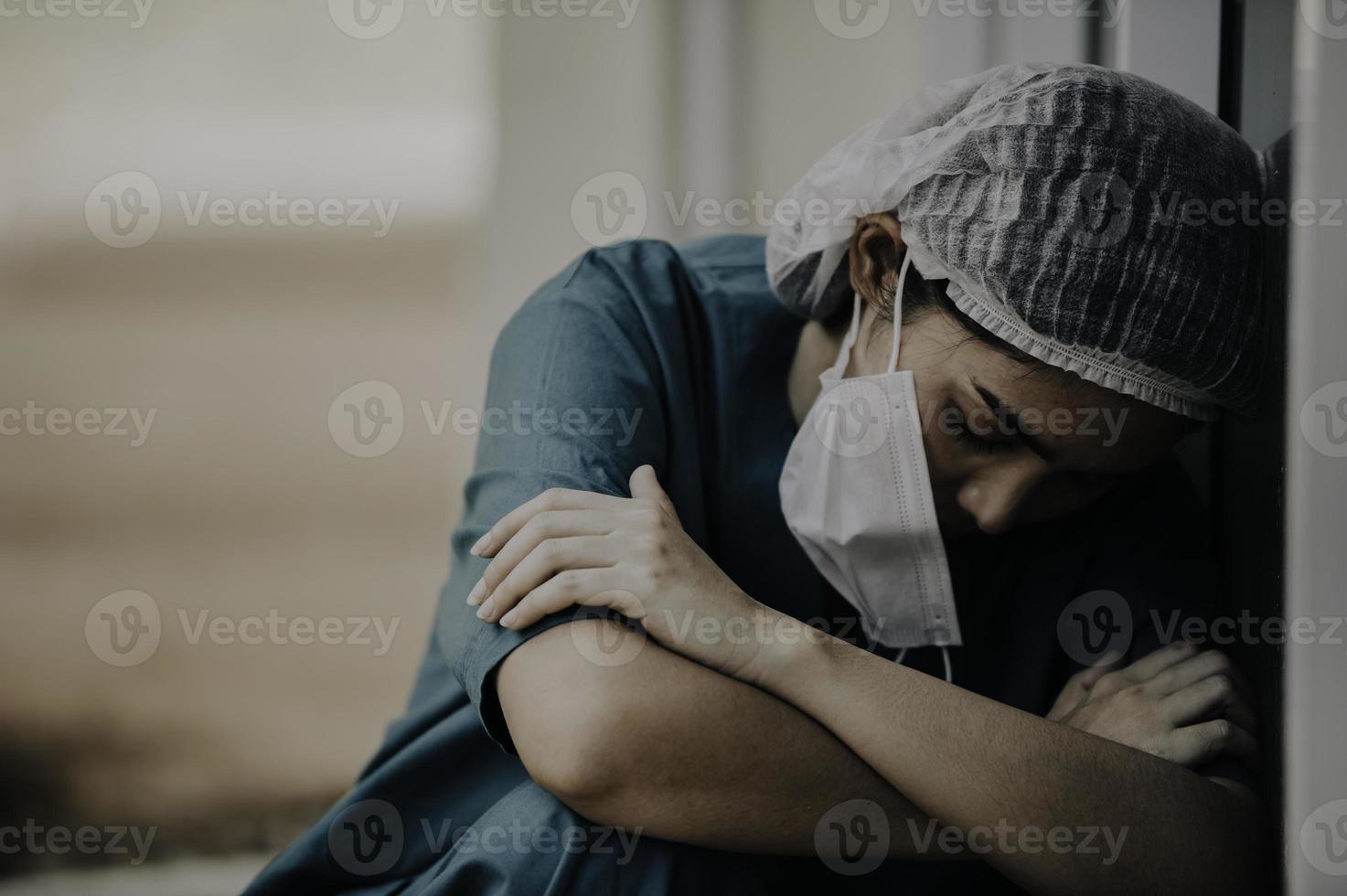 vermoeide depressieve vrouwelijke Aziatische scrubverpleegster draagt gezichtsmasker blauw uniform zit op de ziekenhuisvloer, jonge vrouwelijke arts gestrest van hard werken foto