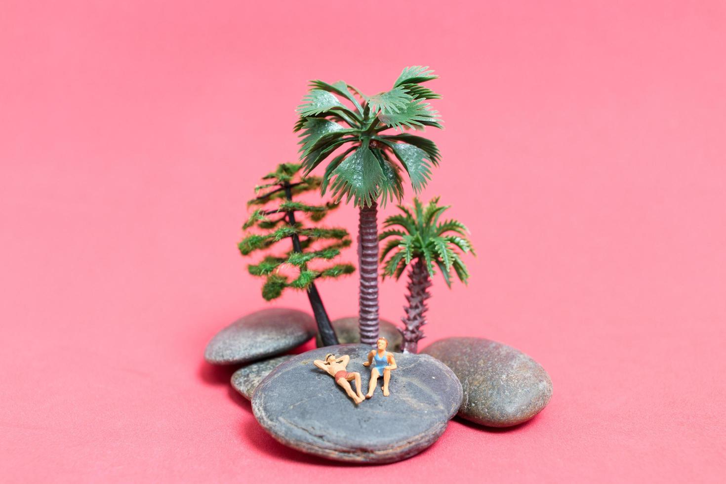 miniatuurmensen die zwemkleding dragen die op een rots met een roze achtergrond ontspannen foto