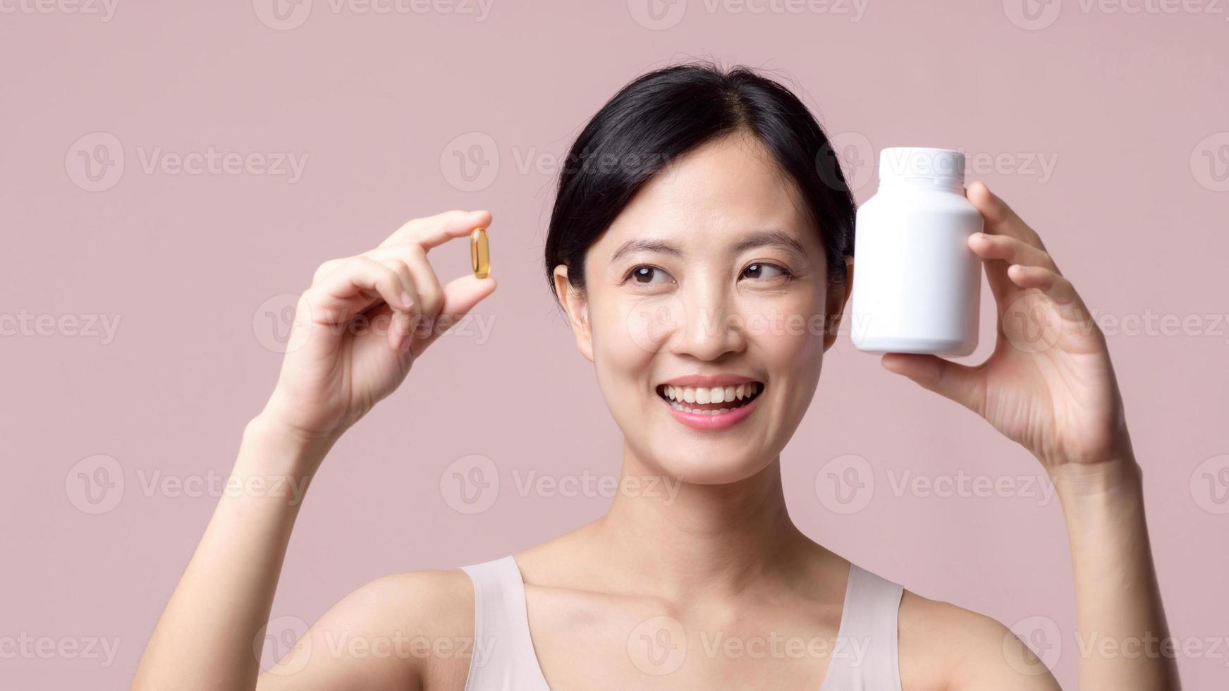 portret jong Aziatisch vrouw gelukkig glimlach gezicht met vitamine voeding pil. mooi schattig meisje vrouw persoon Holding Gezondheid capsule supplement huid zorg geïsoleerd Aan roze achtergrond. geneesmiddel concept. foto